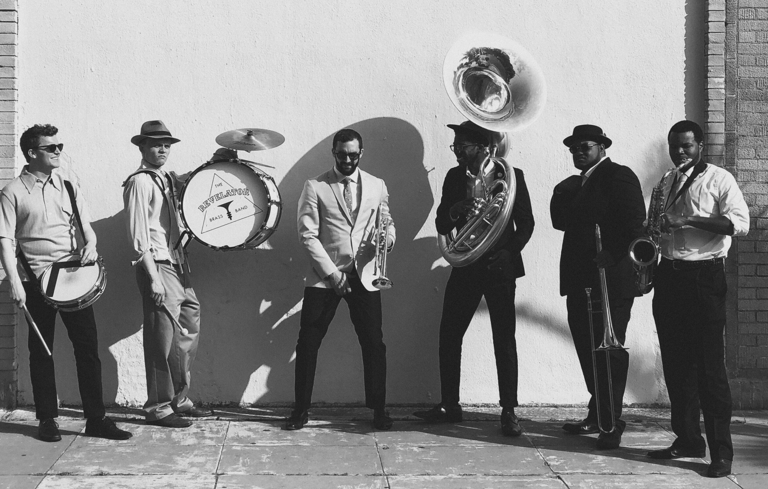 Members of the Revelator Brass Band Stand in front of a wall holding their Second Line instruments.